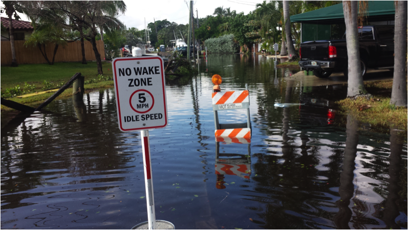 Flooding comes in different forms that can require different solutions. This Fort Lauderdale street with trucks in the foreground and boats in the background illustrates how “king tides” now routinely flood streets. Even a “no wake” sign typically aimed at boats, is intended here to get cars to drive slowly, to minimize salt water waves in the neighborhood (Source: Bob Gremillion, January 2017).